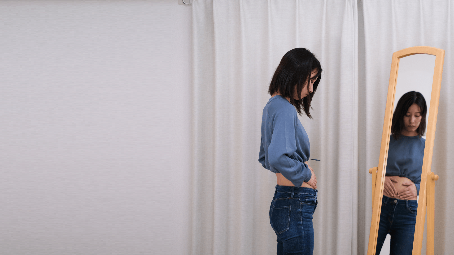 鏡の前で自分の体型を見つめる30代女性
